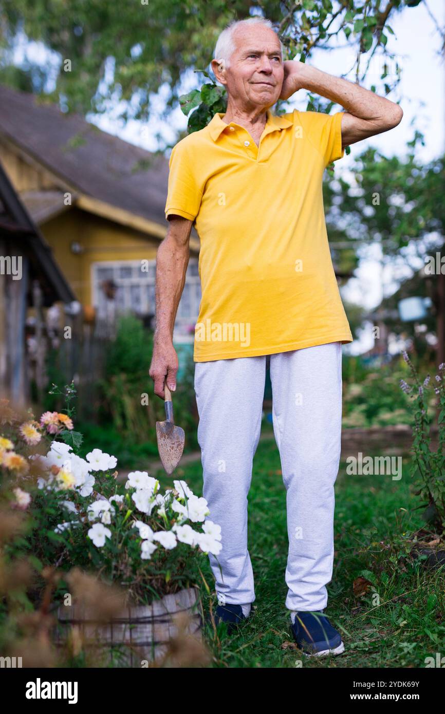 Qualifizierte ältere Arbeiter, die Blumen im Sommergarten pflegen Stockfoto