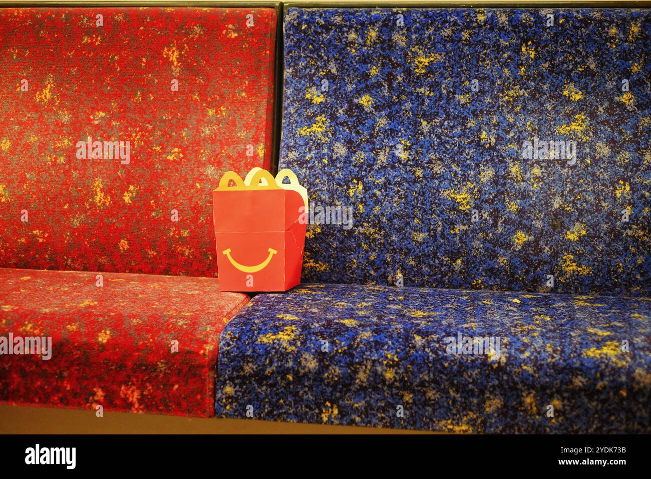 Eine rote McDonalds Happy Meal Box mit einem gelben Lächeln auf den Bahnsitzen, eine rote und eine blaue Stockfoto