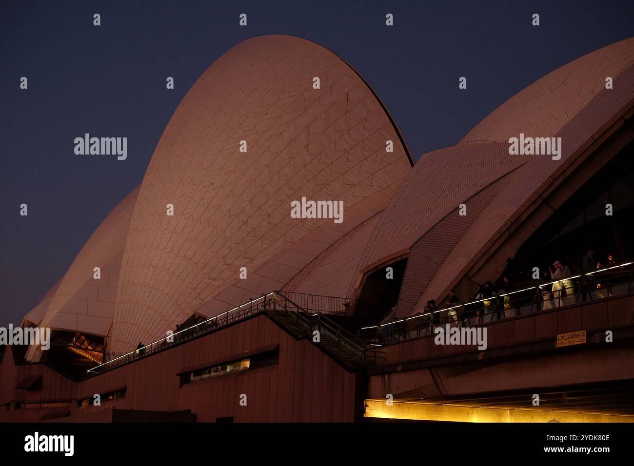 Die hohen Segel der Konzerthalle des Sydney Opera House in der Abenddämmerung mit Menschen auf dem Geländer des oberen Podiums, die nach Osten in den Sonnenuntergang blicken Stockfoto