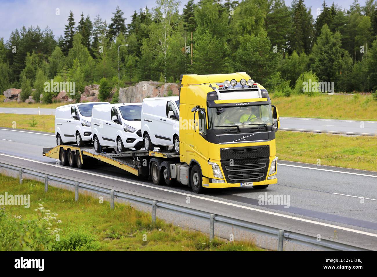 Der gelbe Volvo FH 540 transportiert an einem Sommertag drei weiße Ford-Transporter auf der Autobahn. Salo, Finnland. Juli 2022 Stockfoto