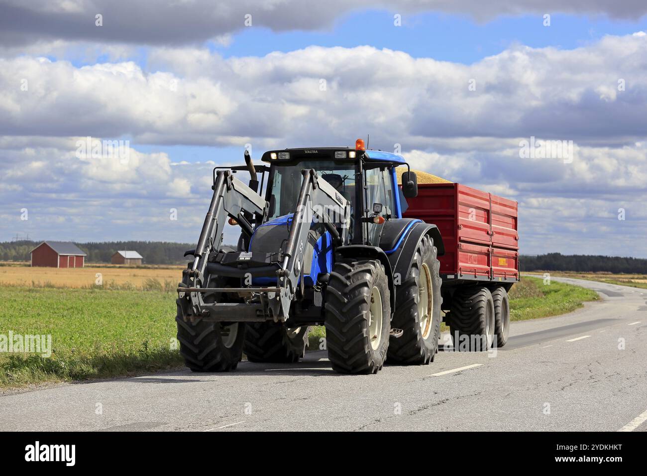 Ilmajoki, Finnland, 11. August 2018: Blauer Valtra-Traktor zieht an einem klaren Herbsttag die Ladung des Erntegutes auf dem Anhänger entlang der Landstraße. Stockfoto