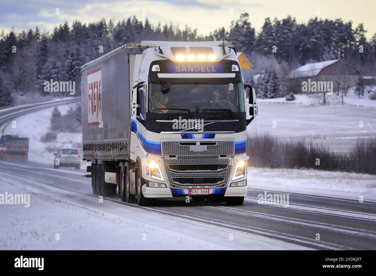 Blauweißer Volvo FH Auflieger Kuljetusliike Harri Sandell Oy mit hellen Scheinwerfern auf der Straße 52 in der Winterdämmerung. Salo, Finnland. Dezember 2021 Stockfoto