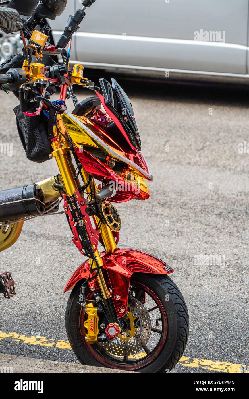 Die Vorderseite eines goldfarbenen Elektrofahrrads oder Rollers, der am Straßenrand im Verkehr von Singapur geparkt ist Stockfoto