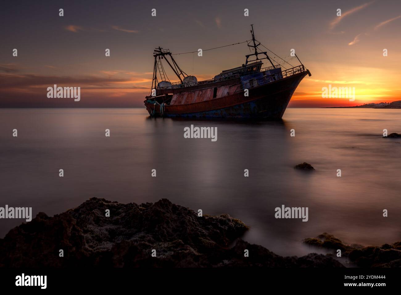 Sonnenuntergang an der Küste von Apulien, Italien, in der Nähe von Tarent. Lange Exposition mit dem Wrack eines größeren Fischerbootes mit einem wunderschönen Himmel. Süditalien Stockfoto