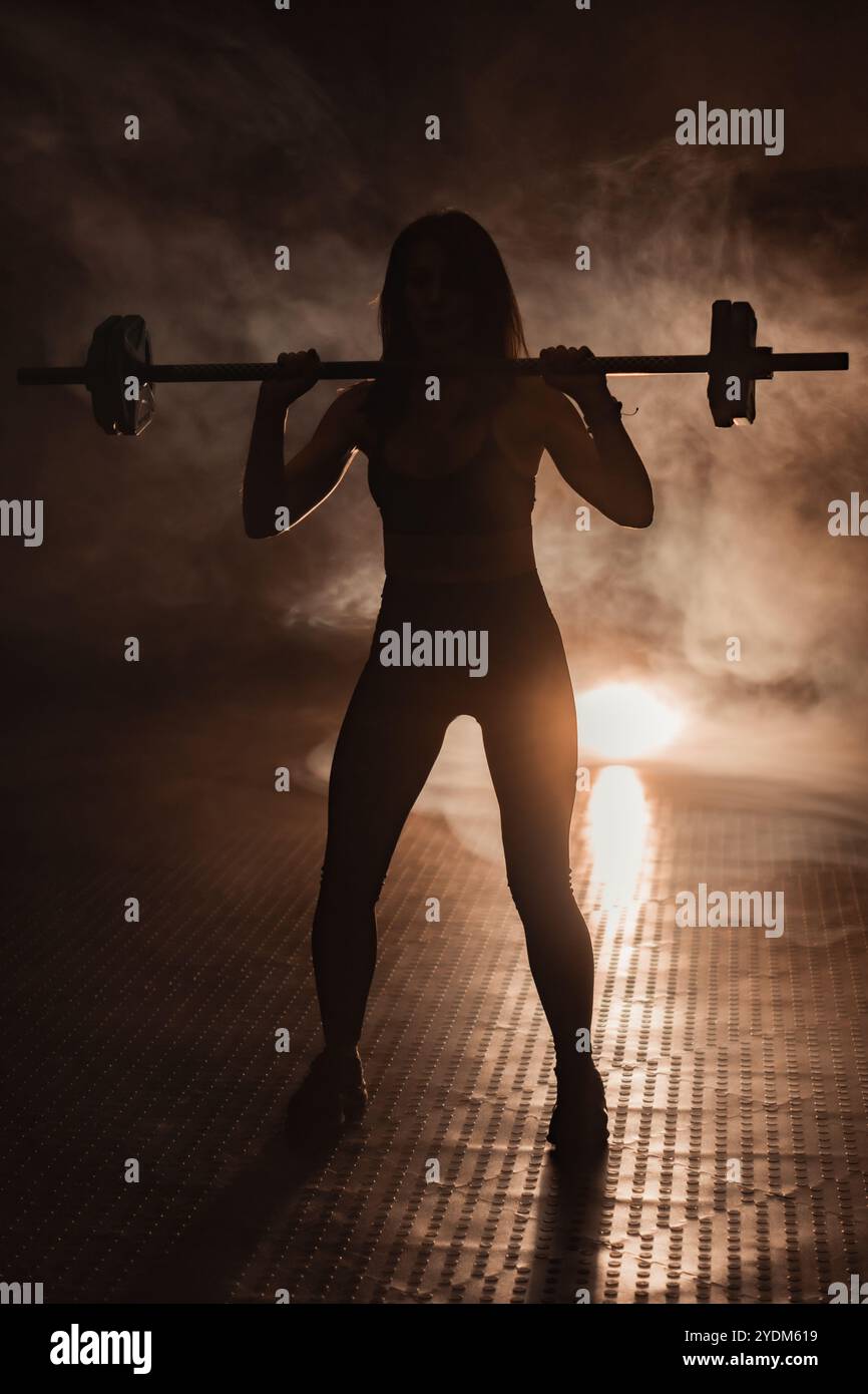 Eine kraftvolle Silhouette einer entschlossenen Gewichtheberin in einem dynamischen Fitnessstudio symbolisiert Sportlichkeit, Mut und Ausdauer und verkörpert den Geist von Stockfoto