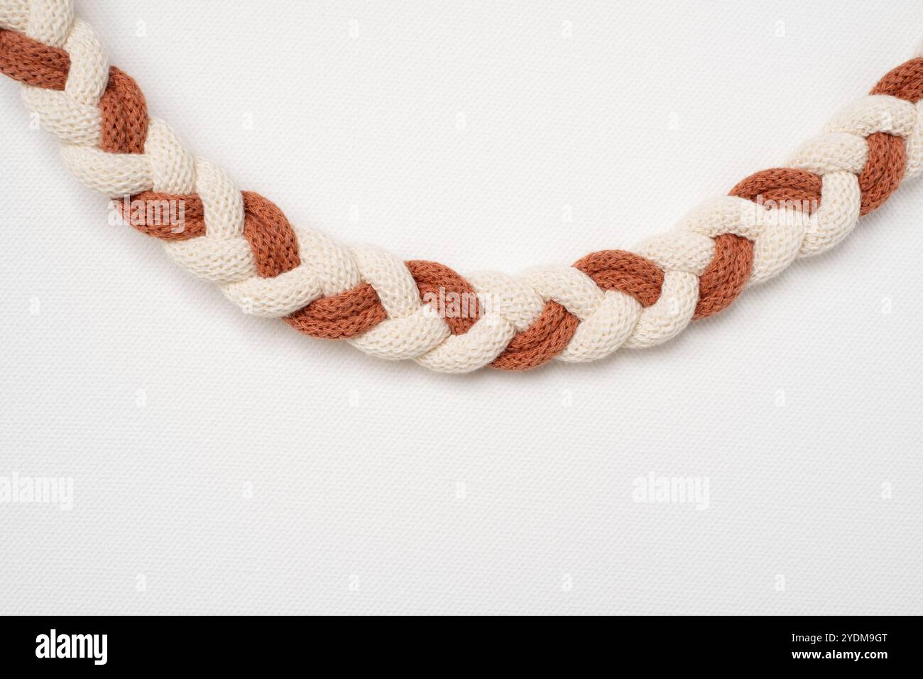 Geflochtene Makramee-Kabel. Weißes und braunes Makramee-Garn, das zu einem Zopf zusammengebunden ist Stockfoto
