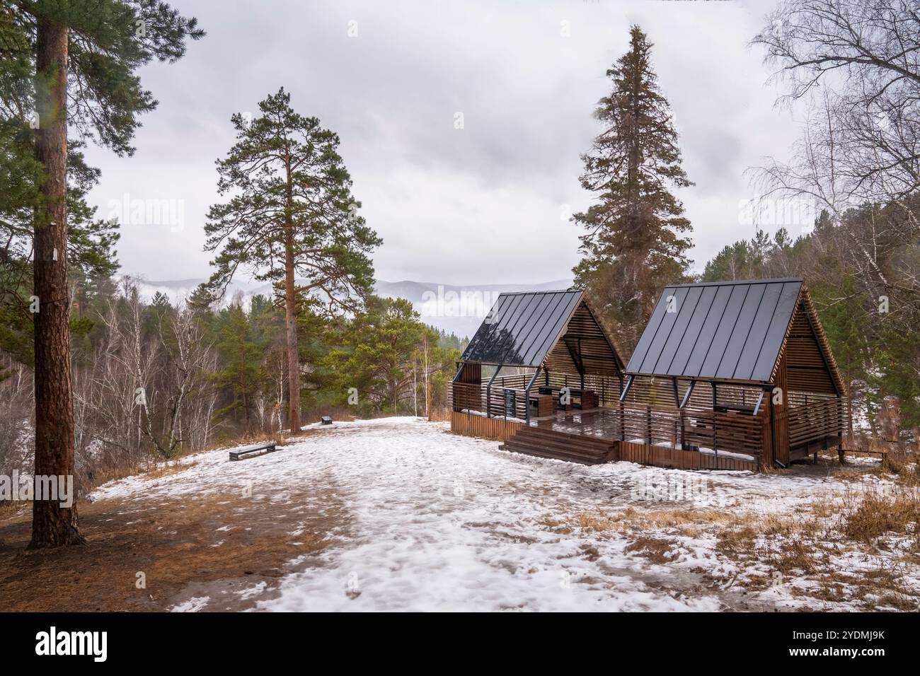 Schneebedeckte Landschaft mit rustikalen Unterkünften und Bäumen, perfekt für ein ruhiges Picknick im Winter oder einen Rückzugsort in der Natur. Gremyachaya Griva Park, Russland Krasnojarsk Stockfoto