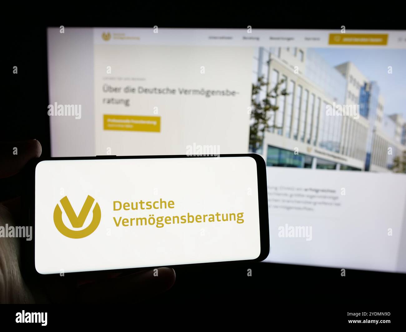 Person mit Mobiltelefon mit Logo der Deutschen Vermögensberatung AG (DVAG) auf dem Bildschirm vor der Webseite. Schwerpunkt auf dem Display des Telefons. Stockfoto