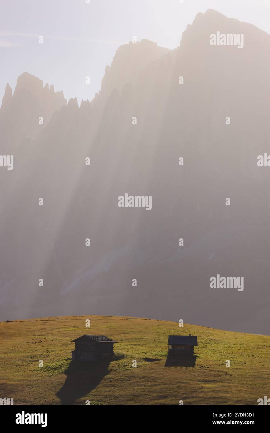 Rustikale Berghütten und Hütten eingebettet in die Almwiesen der Seiser Alm, mit majestätischen Dolomitengipfeln im Hintergrund unter Sonnenstrahlen Stockfoto