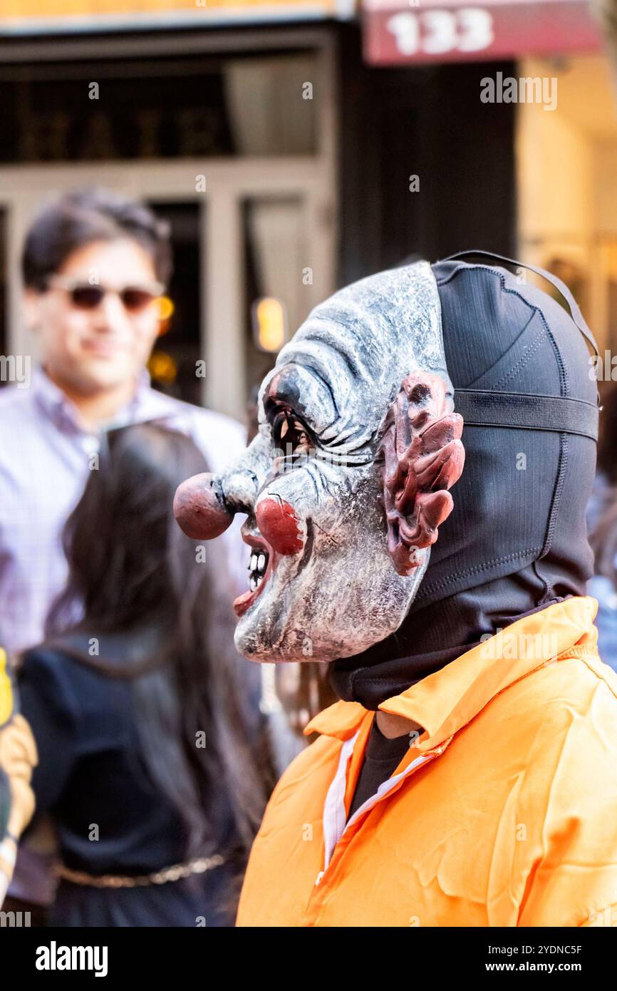 Eine Person mit einer gruseligen Clown-Maske steht in einer lebhaften New yorker Straße während eines Festivals oder einer Hundeparade mit Menschen im Hintergrund Stockfoto