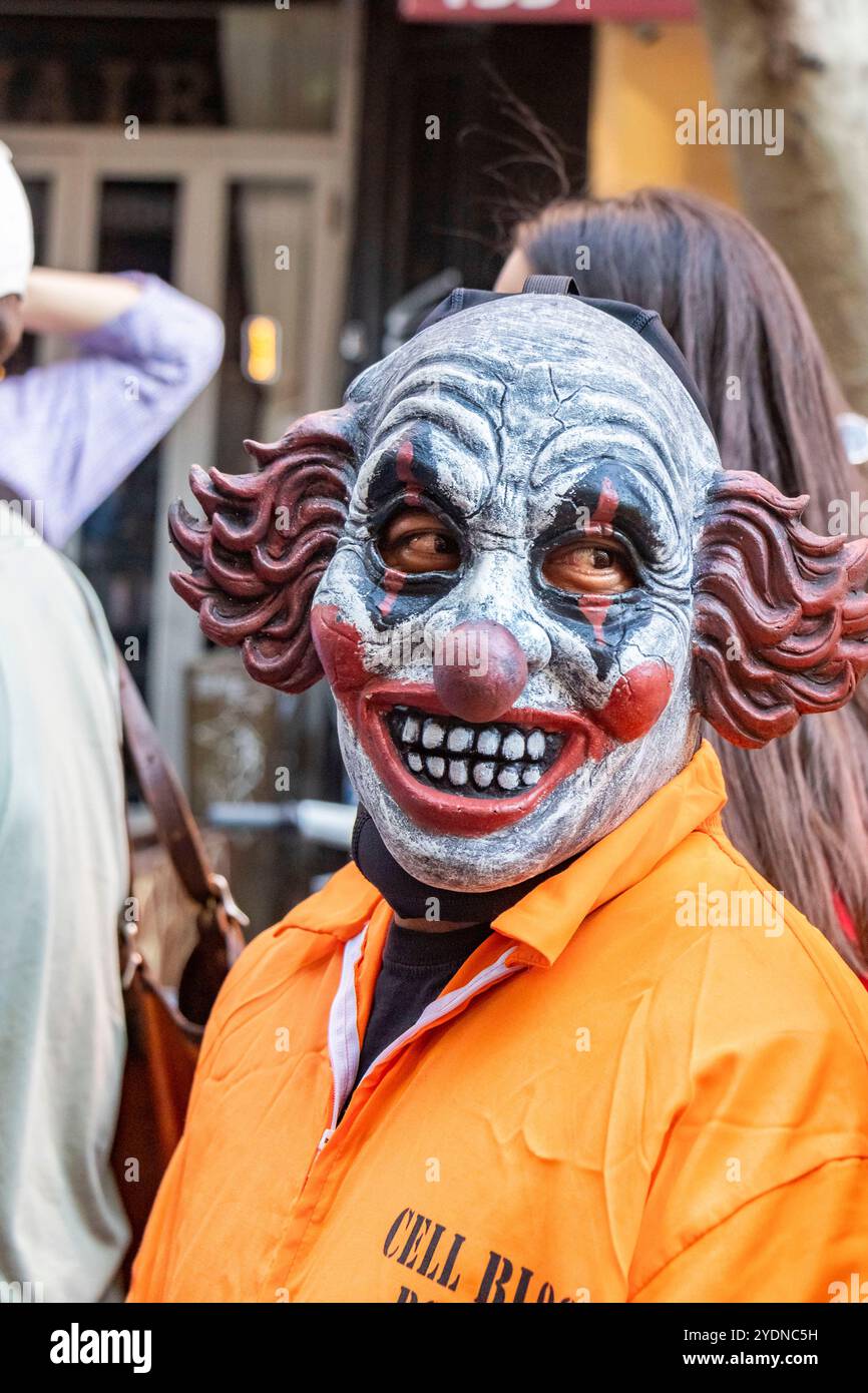 Eine Person mit einer gruseligen Clown-Maske steht in einer lebhaften New yorker Straße während eines Festivals oder einer Hundeparade mit Menschen im Hintergrund Stockfoto