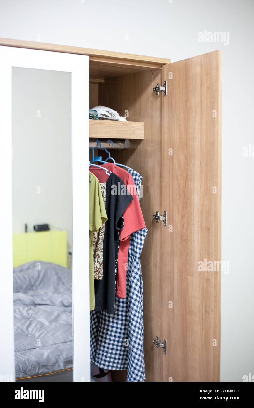 Holzschrank mit Spiegel und offener Tür, Kleidung auf Kleiderbügeln im Kleiderschrank. Stockfoto