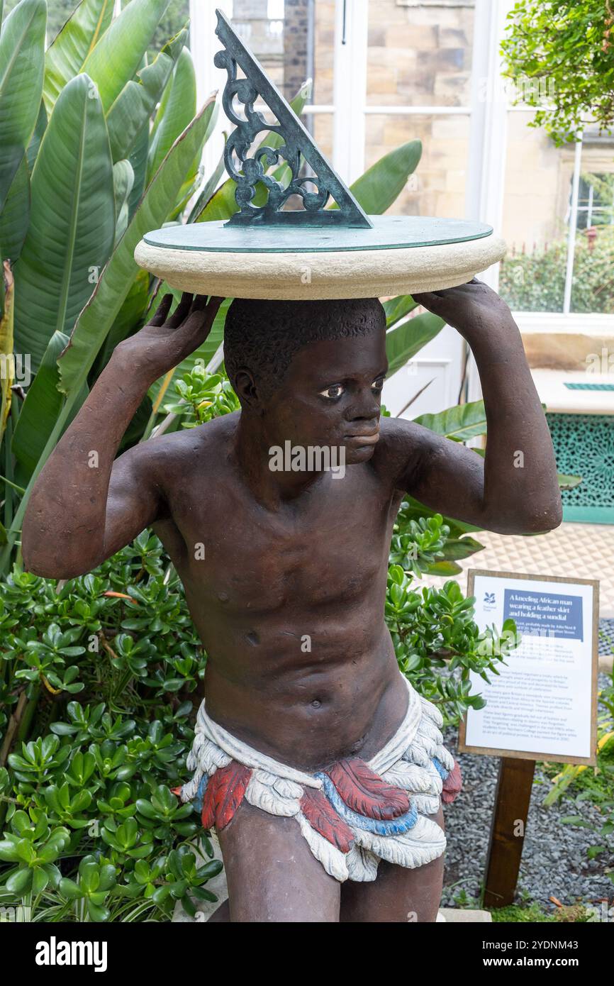 Eine kniende afrikanische Männerstatue in einem Federrock mit einer Sonnenuhr und einer Erklärung der Versklavung in Wentworth Castle Gardens, Yorkshire, England Stockfoto