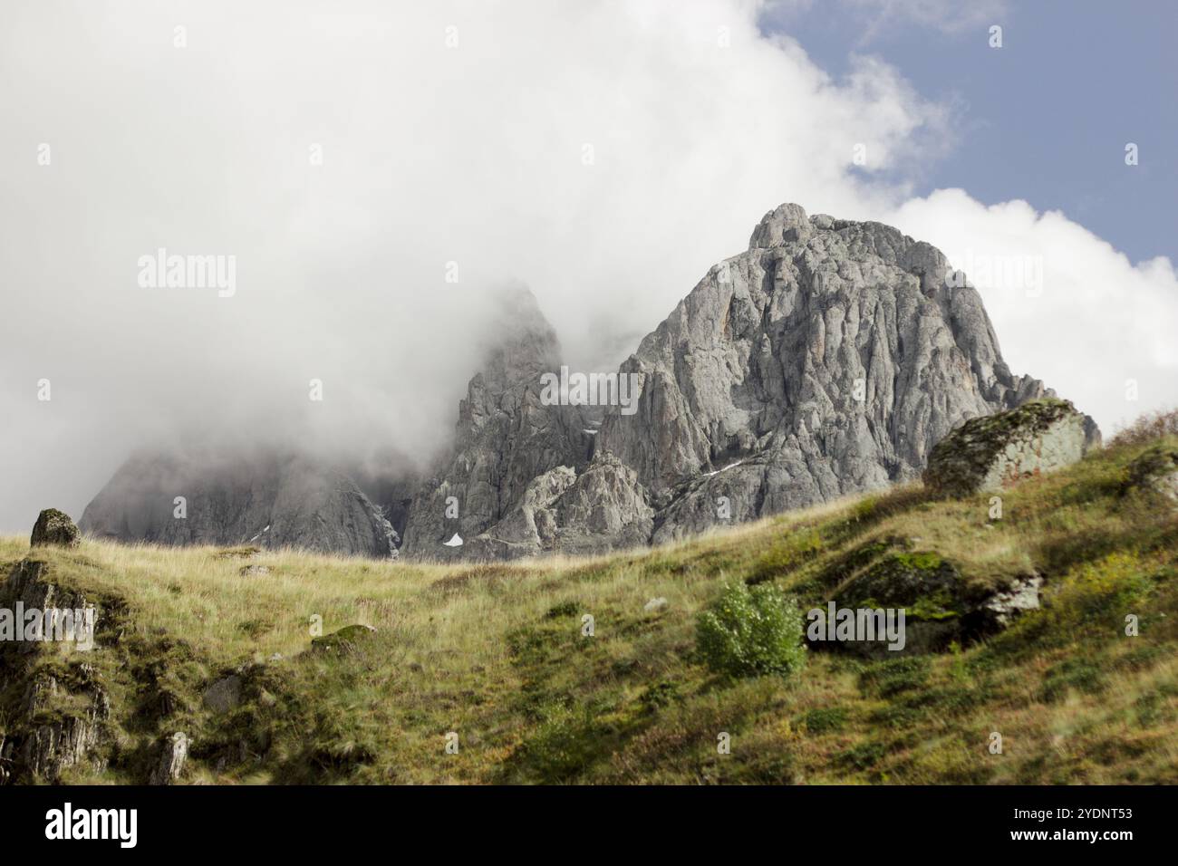 Ein dramatischer Blick auf hoch aufragende felsige Berge, deren Gipfel teilweise von dicken Wolken verborgen sind, die der Szene eine geheimnisvolle Atmosphäre verleihen. Stockfoto