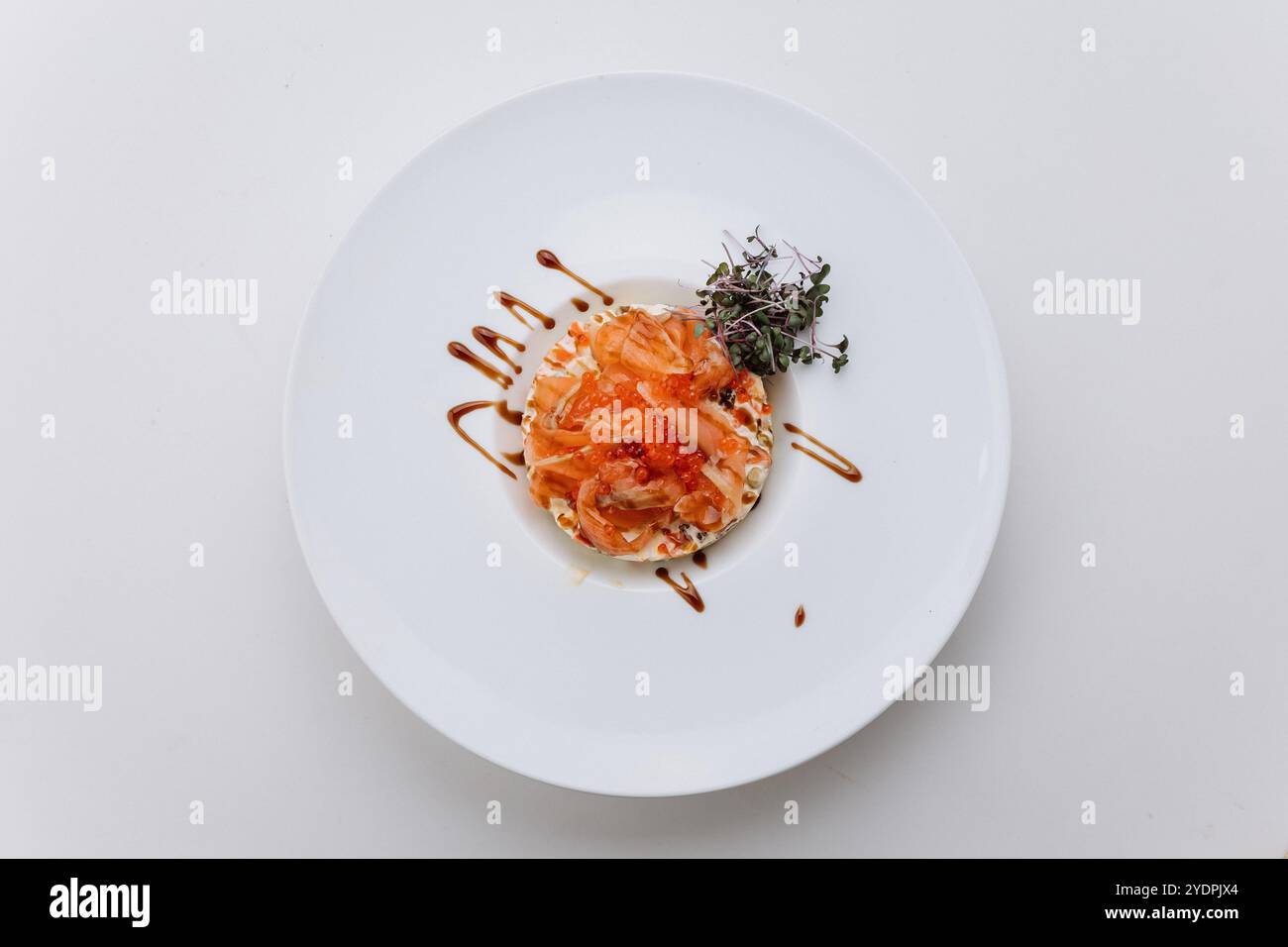 Gourmet-Lachs-Tartar mit rotem Kaviar, Kräutern und Sauce auf einem weißen Teller, raffinierte kulinarische Köstlichkeiten Stockfoto