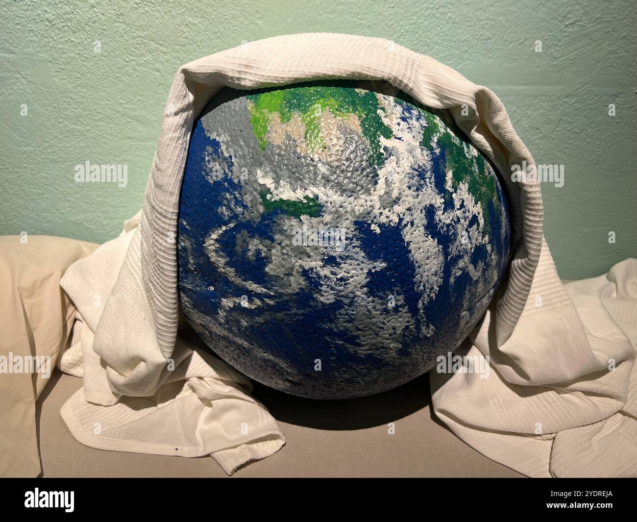 Die Kunstinstallation zeigt den Planeten Mutter Erde ist müde und braucht eine Pause. Decken Sie sich mit einer weißen Decke ab, um sich auszuruhen und zu heilen. Umweltbelange weltweit. - Smartphone-aufgenommenes Stockfoto