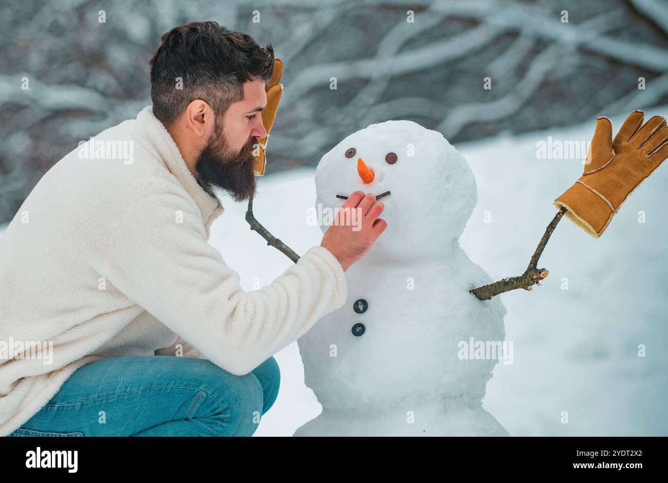 Schneemann und Winterspaß für den Menschen. Wintermann. Glücklicher Vater, der mit einem Schneemann auf einem verschneiten Winterspaziergang spielt. Junge Hipster-Winterporträt. Stockfoto