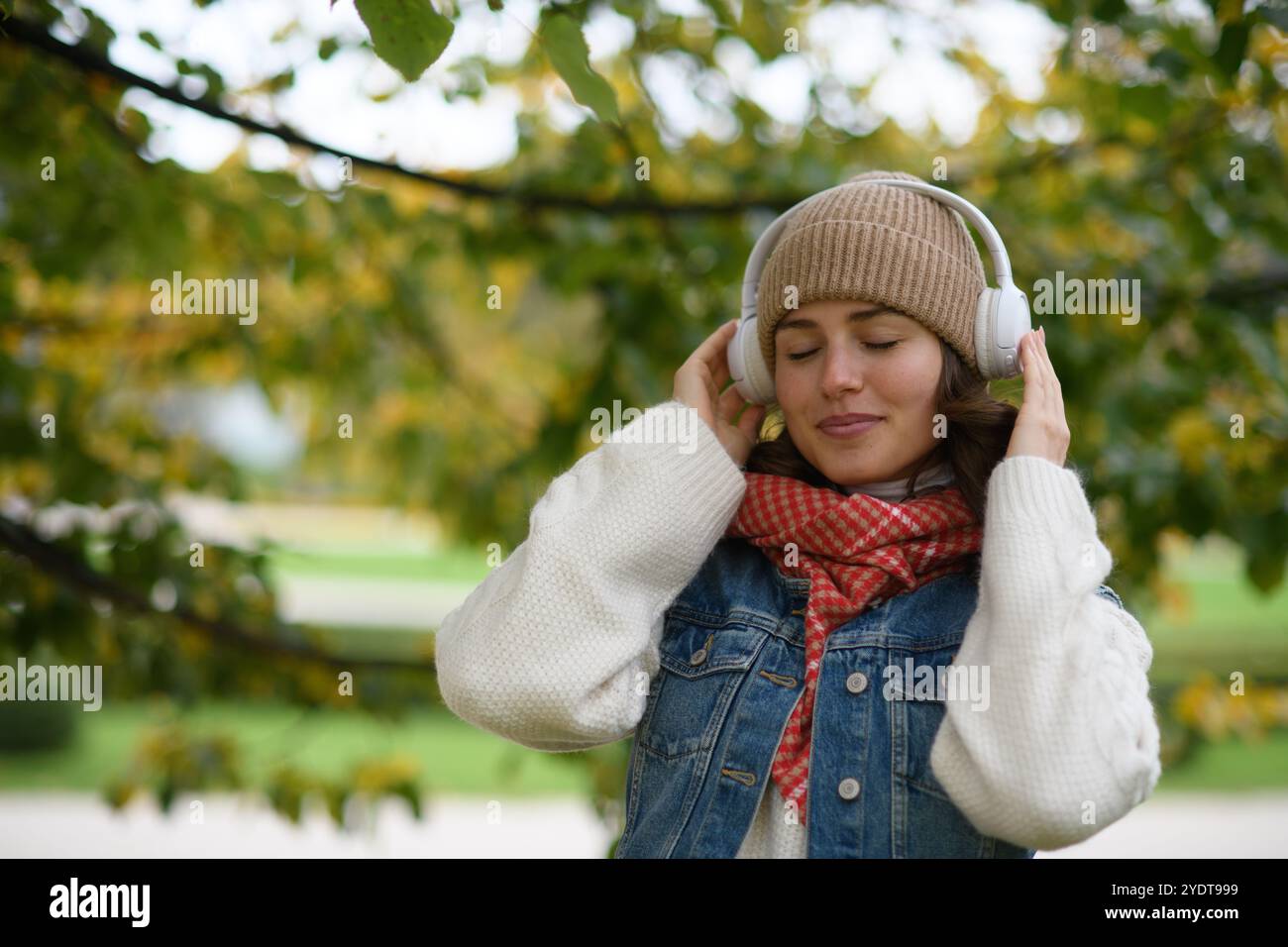 Schöne junge Frau, die im Herbstpark spaziert, Musik hört und einen friedlichen Moment für sich selbst genießt. Stockfoto