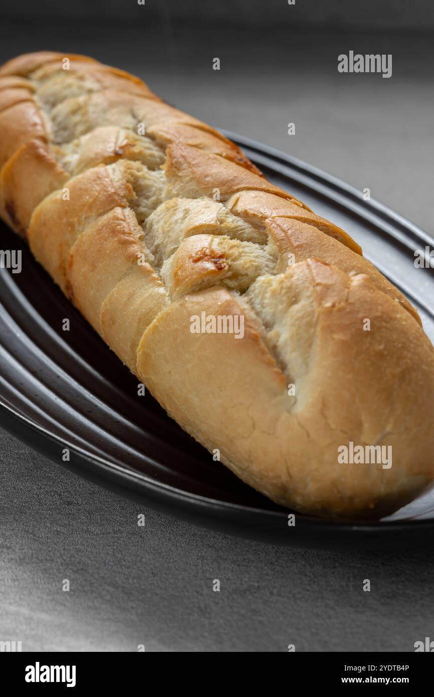 Hausgemachtes Knoblauchbrot-Baguette, vorgeschnitten auf einem schwarzen Steingut-Teller. Auf einer grauen Arbeitsfläche. Stockfoto