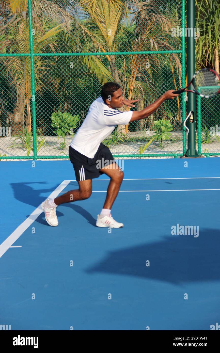 Randheli, Malediven - 24. Februar 2014: Ein asiatischer Indianer spielt Tennis auf einem tropisch blauen Tennisplatz. Stockfoto