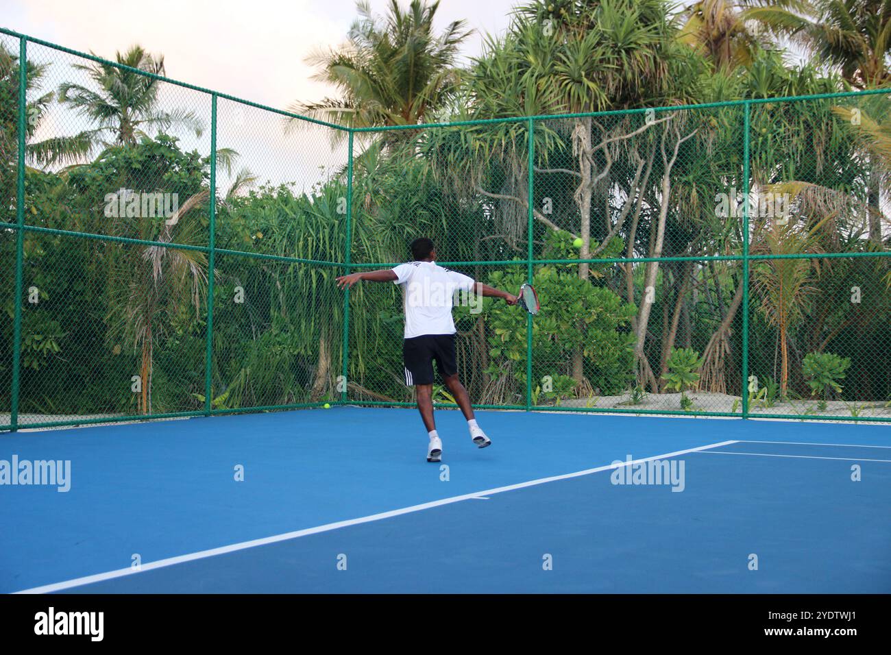 Randheli, Malediven - 24. Februar 2014: Ein asiatischer Indianer spielt Tennis auf einem tropisch blauen Tennisplatz. Stockfoto