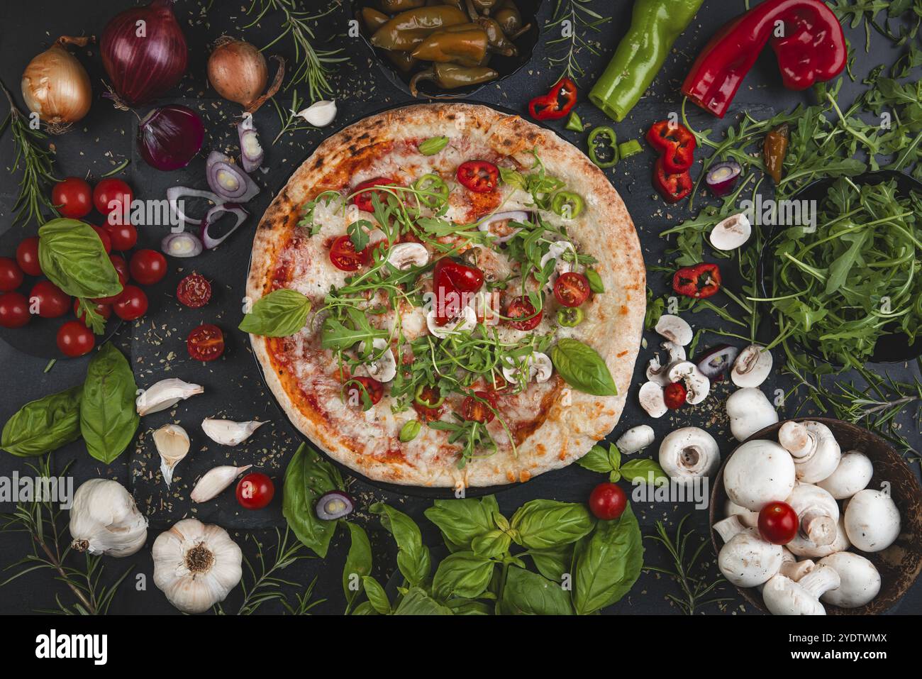 Farbenfrohe Pizza mit Basilikum, Tomaten, Rakete und Pilzen, umgeben von Zutaten Stockfoto