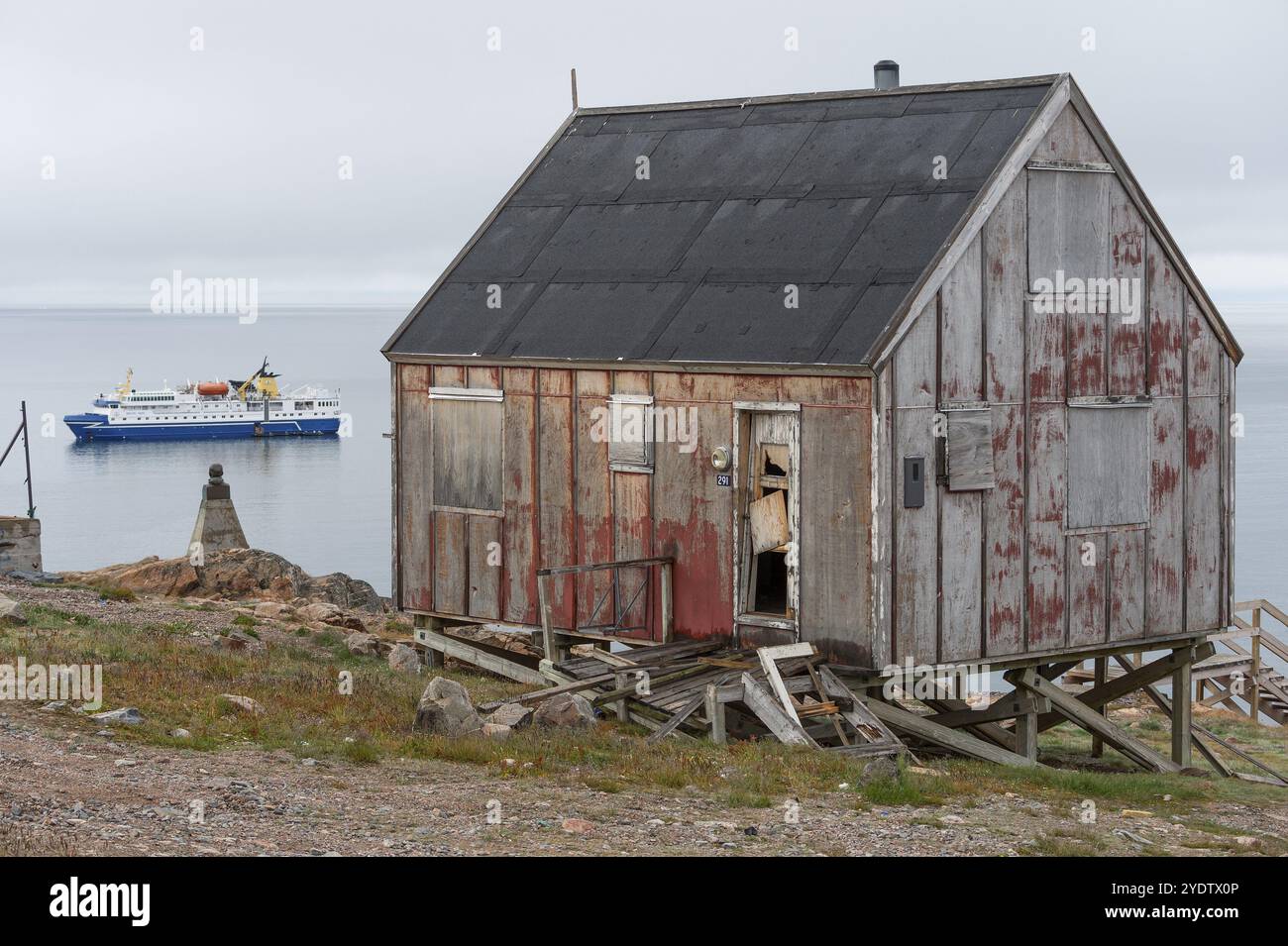 Verfallenes rotes Holzhaus, Expeditions-Kreuzfahrtschiff im Hintergrund, Inuit-Siedlung Ittoqqortoormiit, Scoresbysund oder Scoresby Sund oder Greenlandi Stockfoto