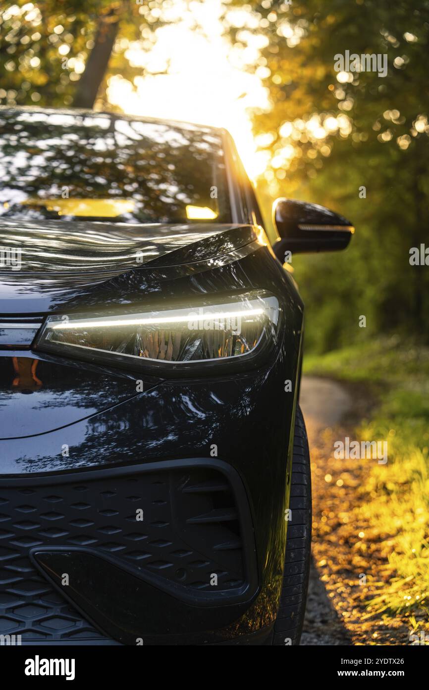 Vorderseite eines schwarzen Autos mit leuchtenden Scheinwerfern, im Hintergrund Sonnenuntergang und Bäume, Elektroauto, VW ID5, Gechingen, Schwarzwald, Deutschland, Europa Stockfoto