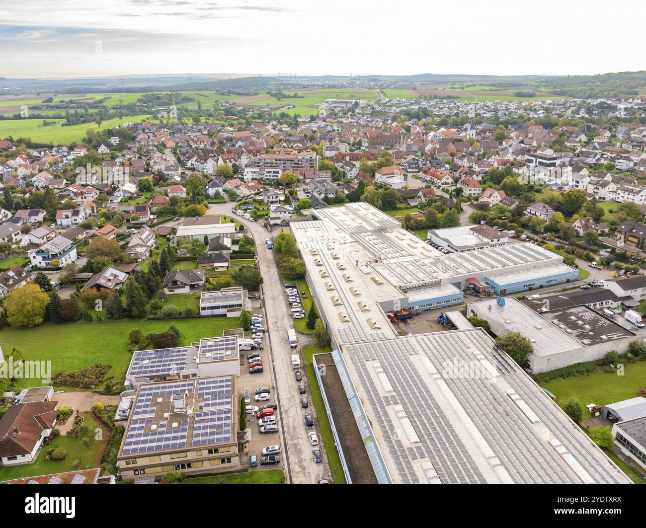 Luftaufnahme einer kleinen Stadt mit Fabrikgebäuden und Wohnhäusern, eingerahmt von grünen Wiesen unter leicht bewölktem Himmel, Wiernsheim, Deutschland, E Stockfoto