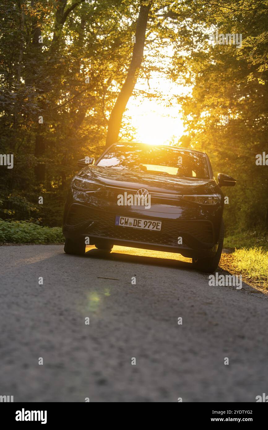 Ein Auto auf einer Straße umgeben von Bäumen, sanftes Sonnenlicht hinter dem Fahrzeug, Elektroauto, VW ID5, Gechingen, Schwarzwald, Deutschland, Europa Stockfoto
