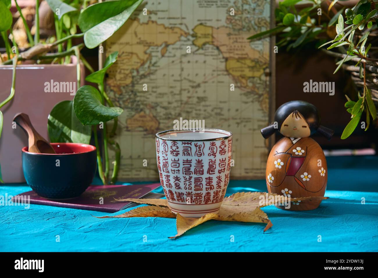 Tee serviert in einer typischen Tasse mit japanischen Ideogrammen, im Hintergrund eine orientalische Holzpuppe und eine kleine Schüssel mit Gewürzen. Szene in einem gar im Freien Stockfoto