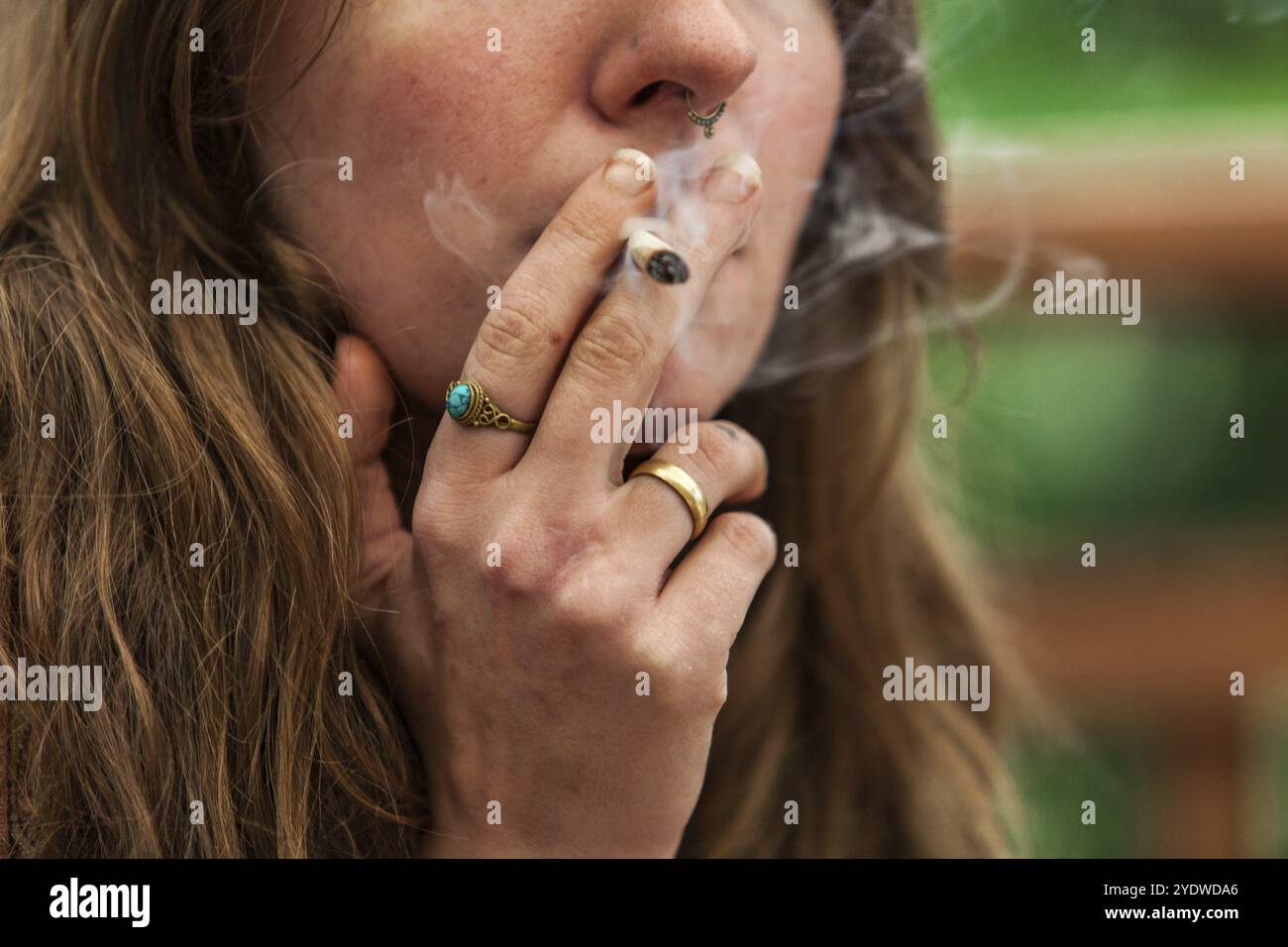 Nahaufnahme 3/4-Schuss kaukasischer Frauen Gesicht mit handgerolltem Marihuana-Gelenk, das von ihrem Ring bedeckt gehalten wird Finger Topf Rauch entweicht aus ihren Lippen Stockfoto