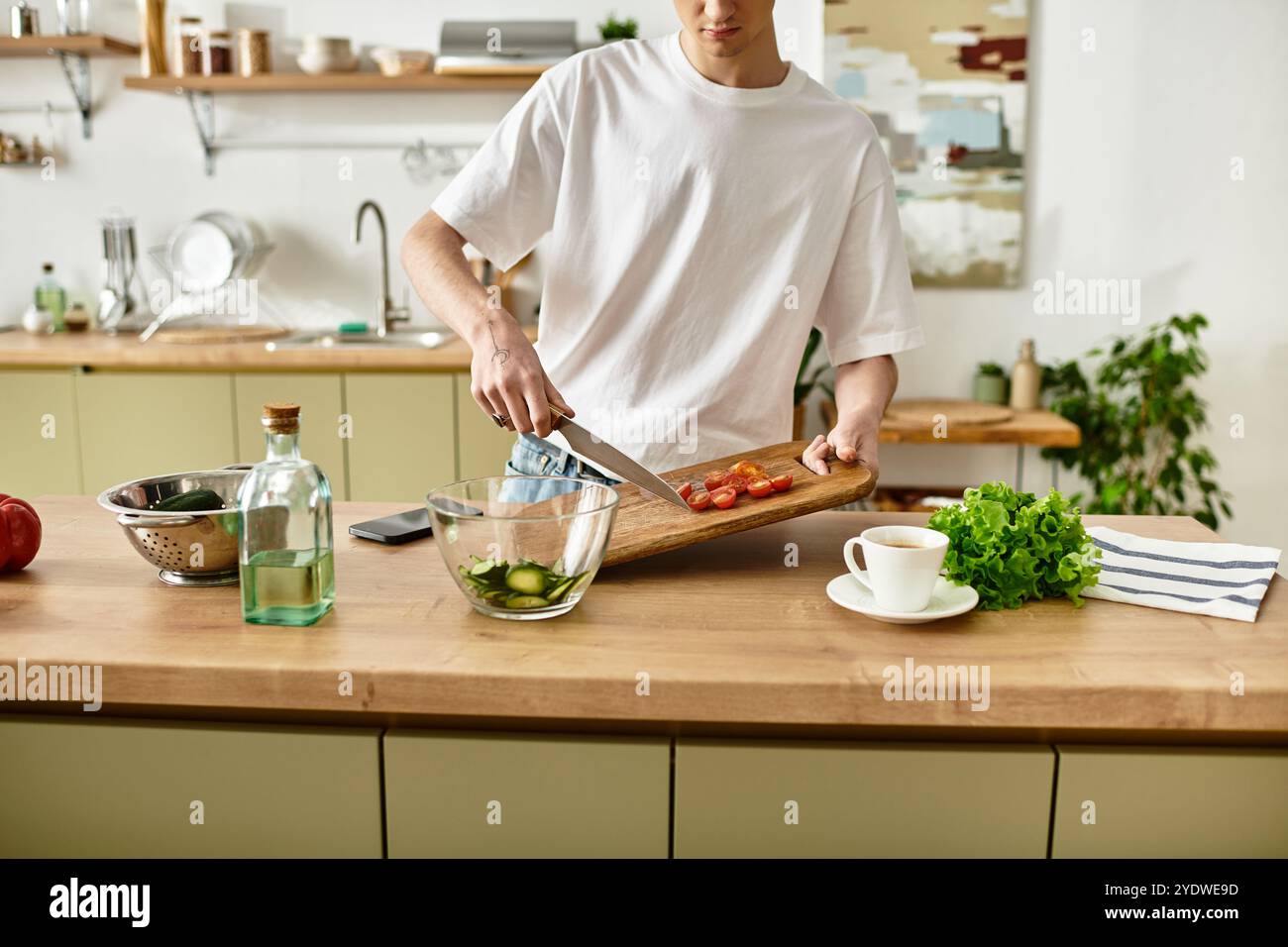 Ein junger Mann hackt gekonnt Gemüse und kreiert einen lebendigen Salat in einer schicken Küche. Stockfoto