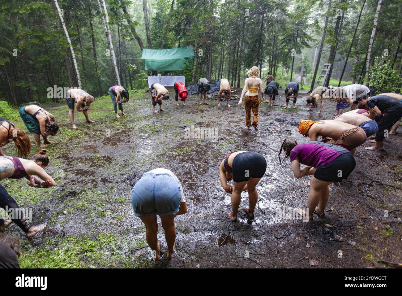 Eine generationenübergreifende Gruppe von Menschen aus allen Hintergründen sieht man im Kreis um einen Yogalehrer stehen, im Utanasana oder in der Vorwärtsbeugung stehen Stockfoto