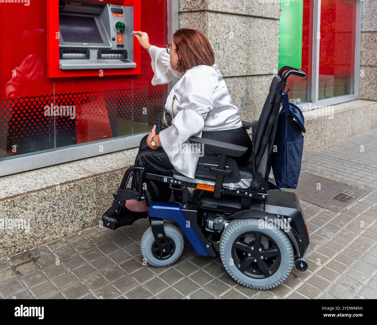 Frau im Rollstuhl, die einen Geldautomaten auf der Straße benutzt Stockfoto