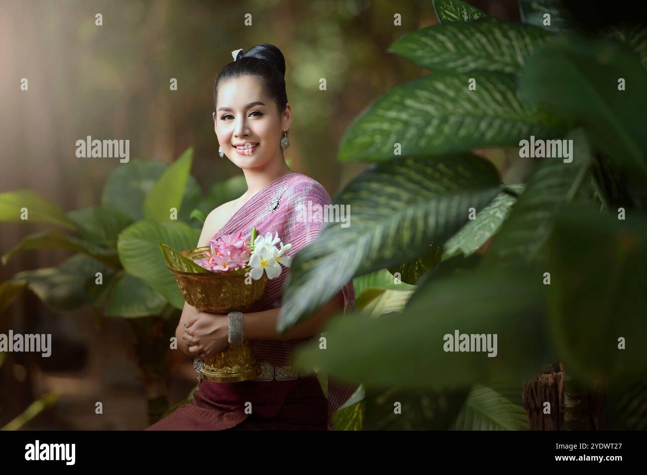 Lächelnde junge Frau in traditioneller laotischer Kleidung im Wald mit einer Schüssel frischer Blumen, Laos Stockfoto