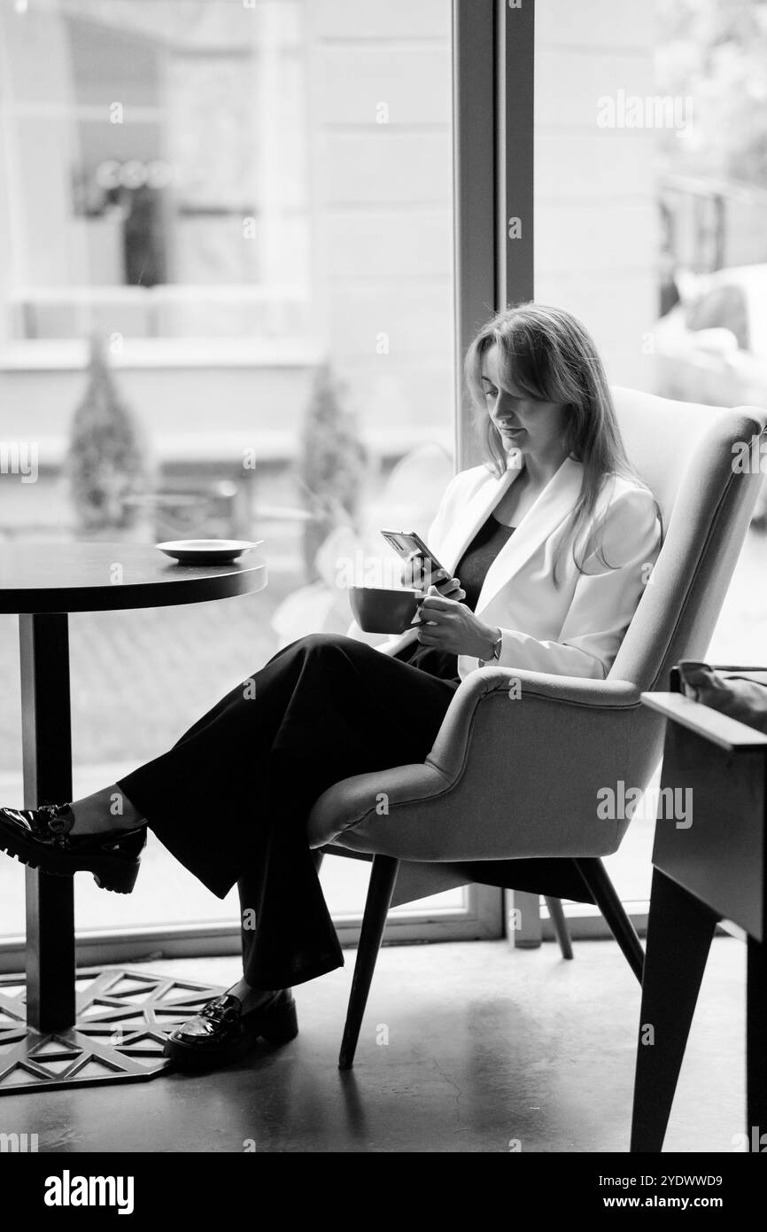 Elegante Frau in einem Café, vertieft in ihr Telefon. Stockfoto