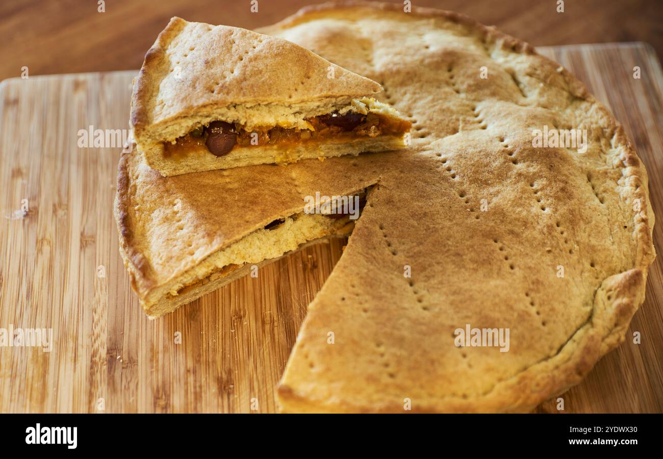 Gebackener Zwiebelkuchen gefüllt mit Oliven, gemischten Zwiebeln und grünen Zwiebeln mit einer goldbraunen Kruste auf einem verbrannten Holzbrett. Focaccia cipolle Stockfoto