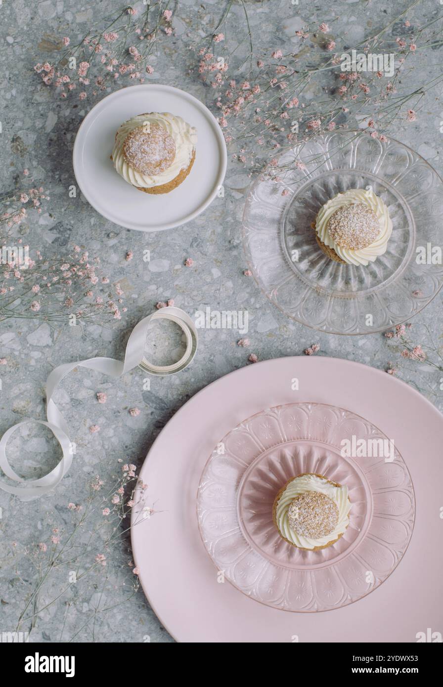 Blick von oben auf verschiedene Teller mit drei Cremekuchen auf einem Tisch, der mit Blumen und Band dekoriert ist Stockfoto