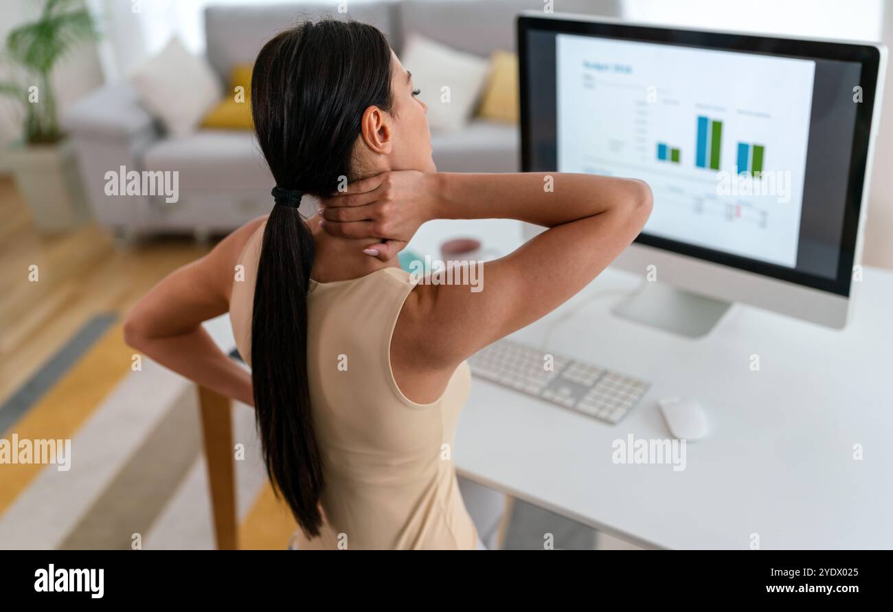 Müde Arbeitnehmerin sitzt am Schreibtisch, Rückenschmerzen leiden, Frau starke Rückenschmerzen, falsche Haltung Stockfoto