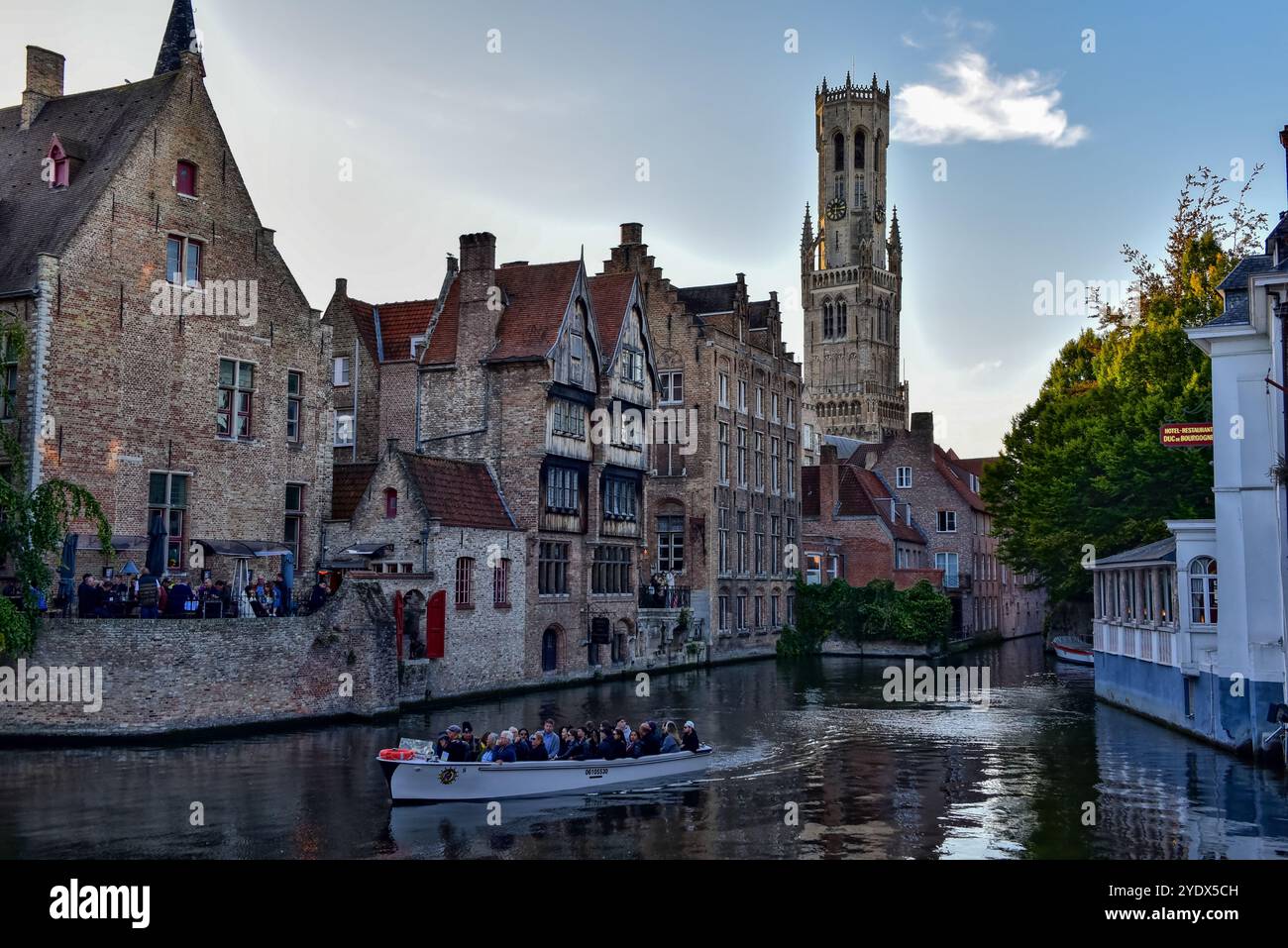 Glockenturm von Brügge, mittelalterliche Backsteinbauten, Kreuzfahrtschiffe und ihre Reflexion auf dem Dijver-Kanal in der Abenddämmerung, vom Rosenkranzquay in Brügge, Belgien. Stockfoto