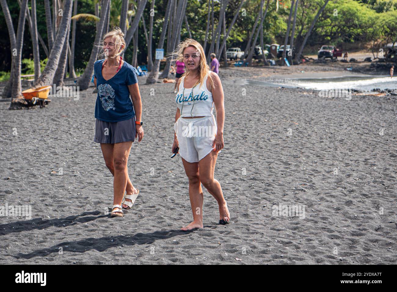 Dieses wunderschöne Bild zeigt eine Mutter und ihre Tochter, die Hand in Hand an der spektakulären Küste des Punalu'u Beach auf Hawaii schlendern. Stockfoto