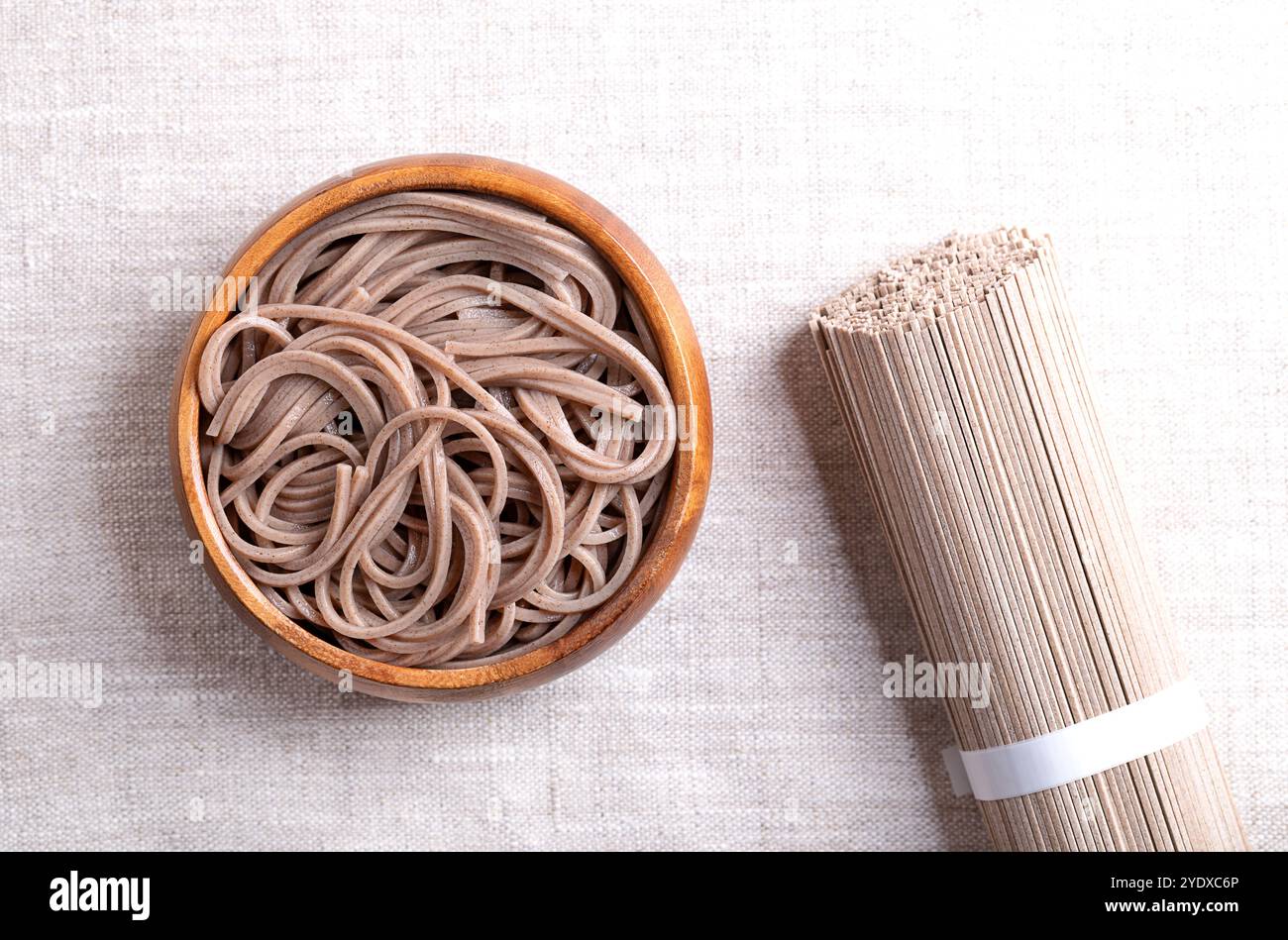 Gekühlte, gekochte Soba-Nudeln in einer Holzschale auf Leinenstoff. Dünne japanische Nudeln, die hauptsächlich aus Buchweizenmehl hergestellt werden, wobei Weizenmehl gemischt wird. Stockfoto