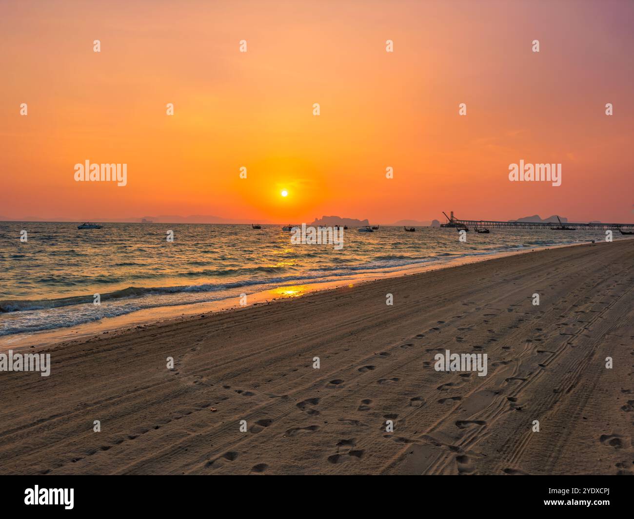 Feurig roter tropischer Sonnenuntergang am Strand Klong Muang in der Provinz Krabi in Thailand. Langschwanzboote im Meer. Stockfoto