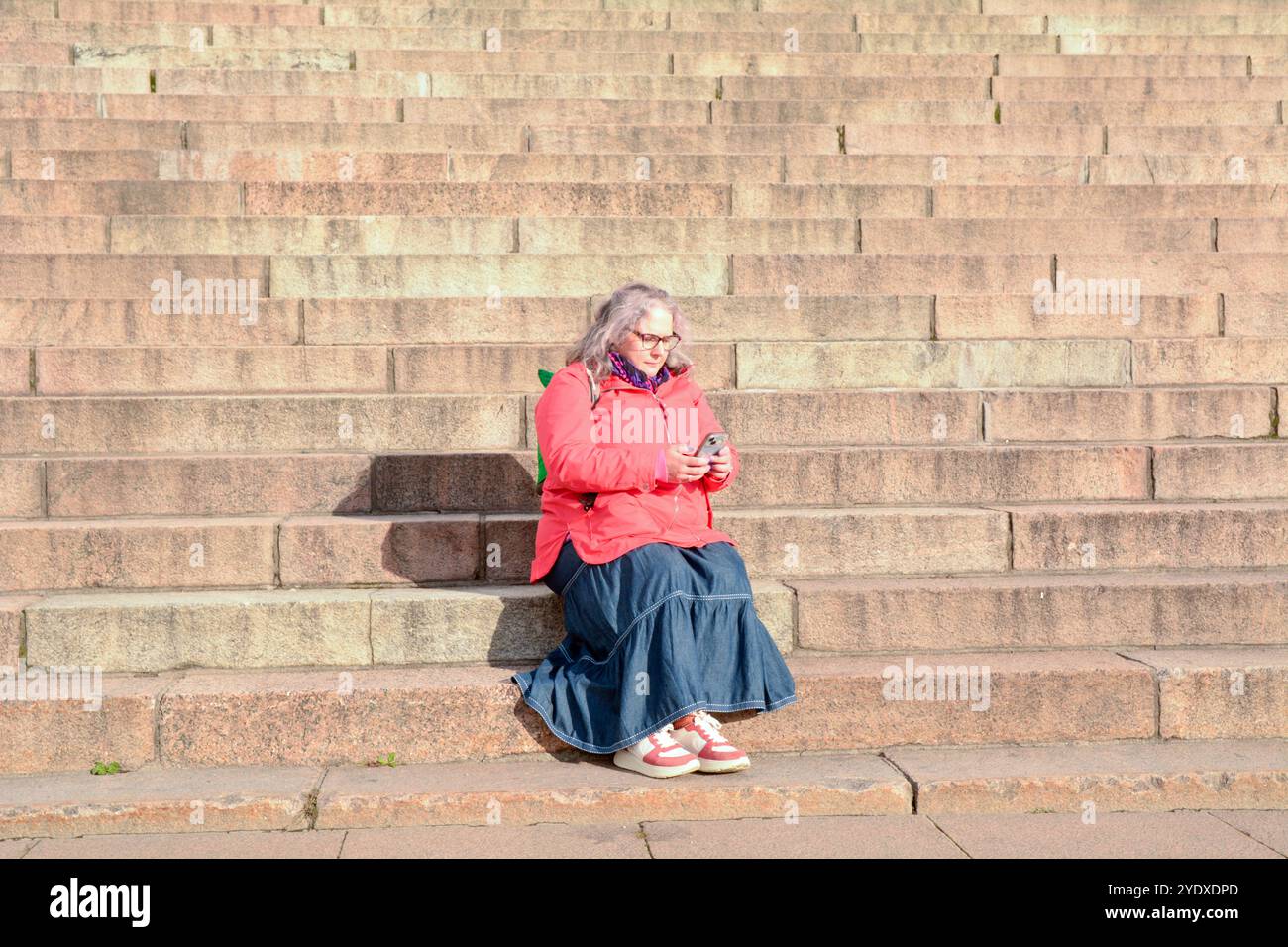 Frau sitzt und überprüft ihr Smartphone auf der Treppe zur Kathedrale von Helsinki (Helsingin tuomiokirkko) auf dem Senatsplatz in Finnland Stockfoto