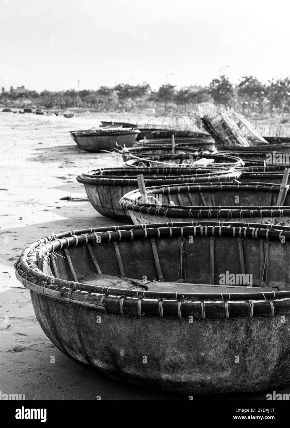 Schwarz-weißes Bild von Korbbooten, einem traditionellen vietnamesischen Fischerboot, das in der Nachmittagssonne an einem Strand angereiht ist. Stockfoto