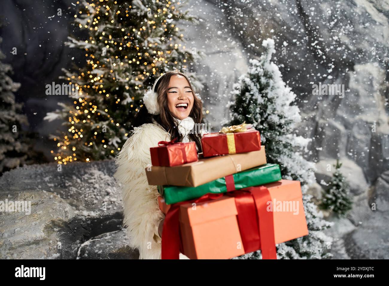 Eine glückliche Frau spaziert durch die verschneite Landschaft und hält fröhlich einen Stapel farbenfroher Weihnachtsgeschenke in der Hand. Stockfoto