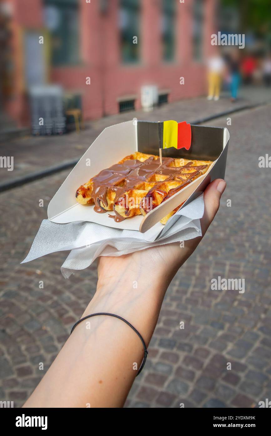 Hand mit einer traditionellen belgischen Lüttich-Waffel mit Schokoladenaufstrich, belgischer Flagge und belgischem Street Food Stockfoto