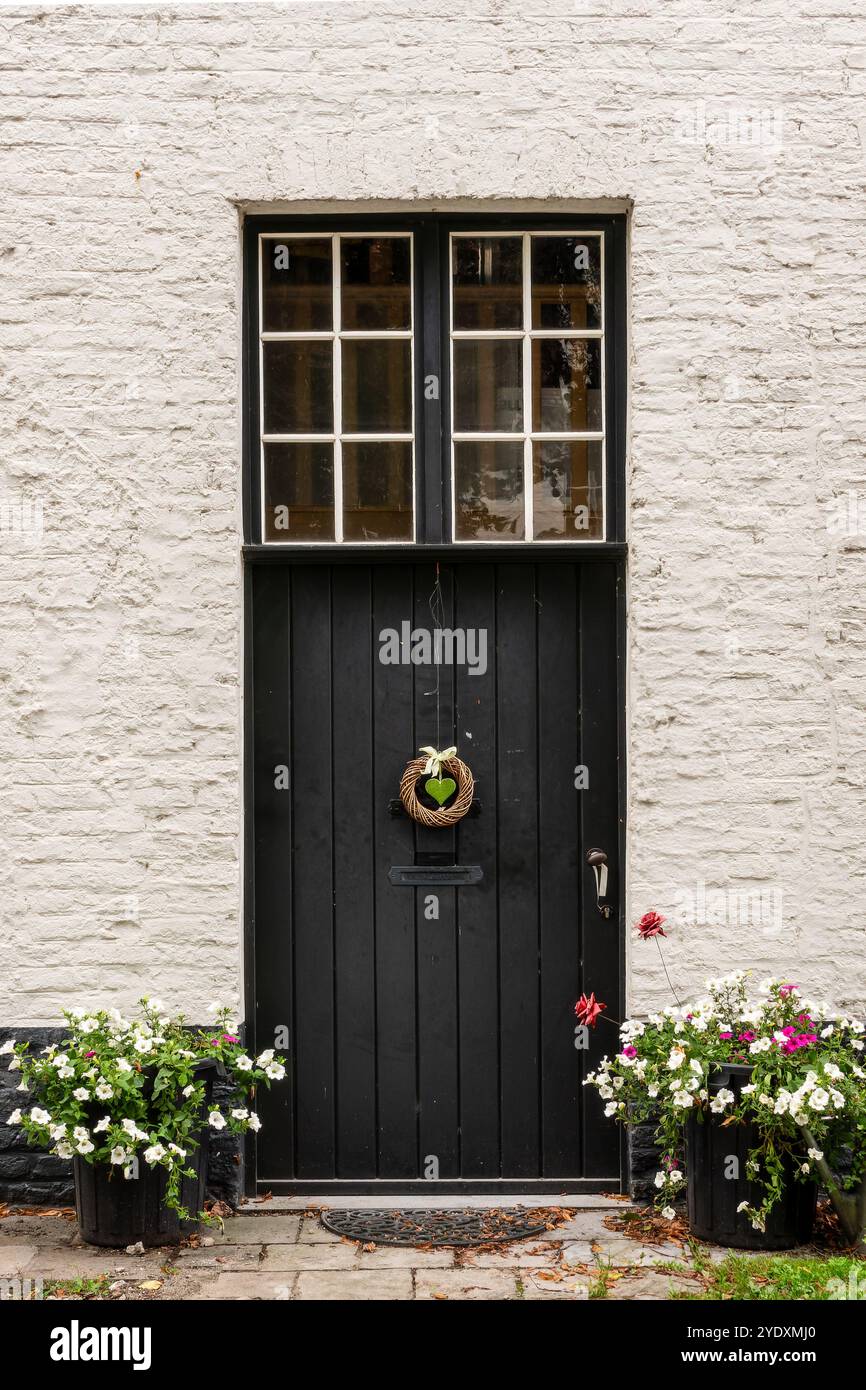 Malerische schwarze Tür mit herzförmigen Ornamenten und Blumentöpfen, mittelalterliche flämische Architektur in Brügge, Belgien Stockfoto