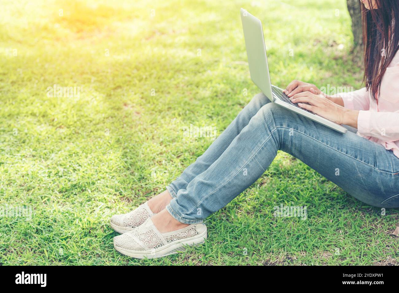 Asiatische Frau, die im grünen Park sitzt und einen Laptop benutzt. Frau, die an einem Laptop arbeitet, glückliches Unternehmerunternehmen, das ein Notebook verwendet, während die Hände auf der Tastatur tippen Stockfoto